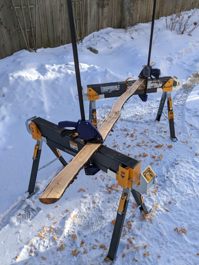 a log being hand-planed on two sawhorses outdoors