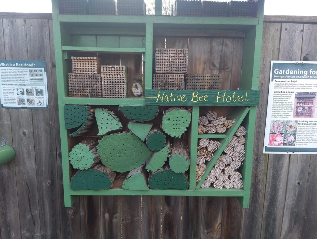 a large green bee hotel labeled "Native Bee Hotel" with many pieces of wood with drilled out holes