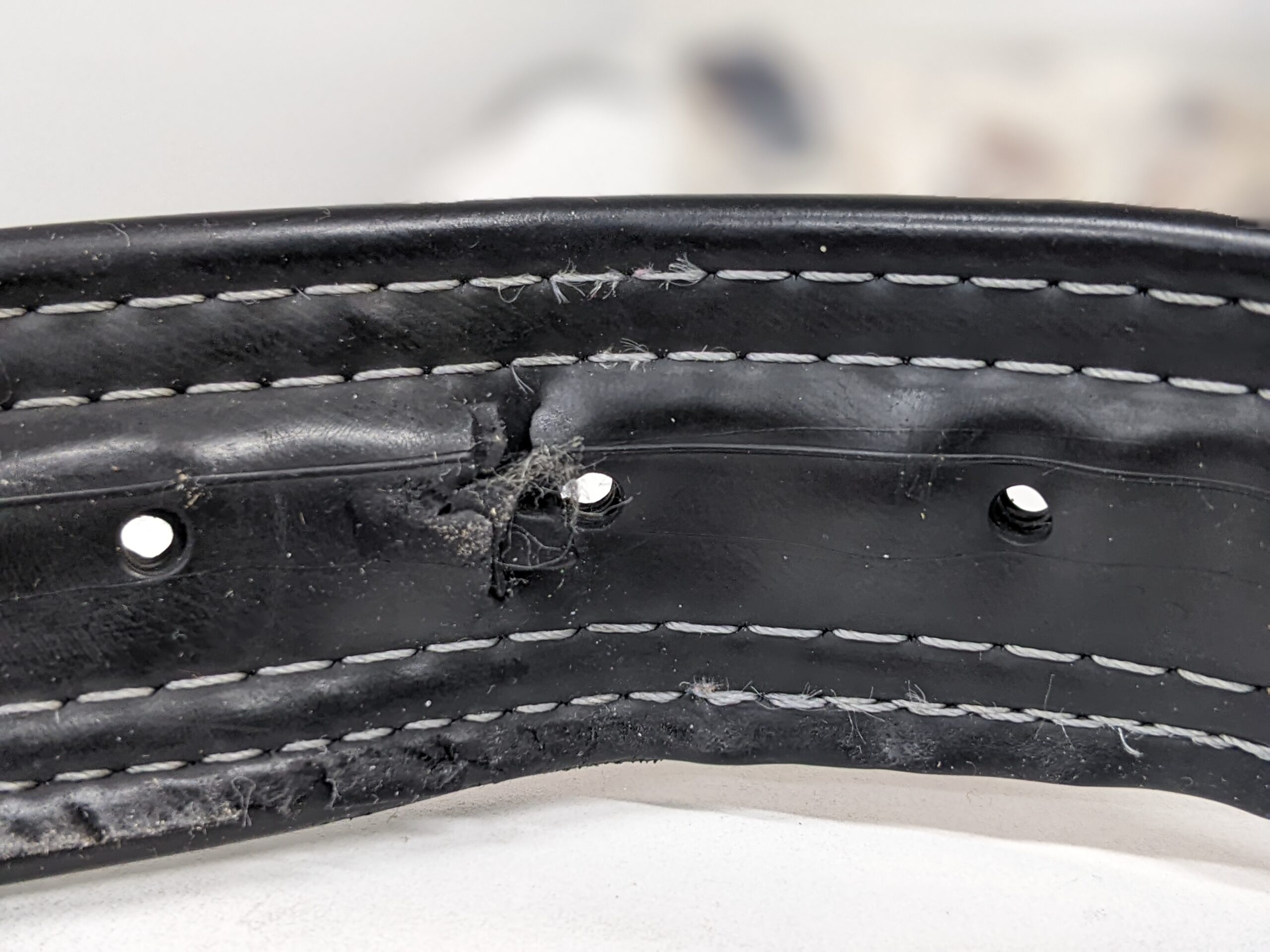 a black belt with white stitching, one of the holes has been stretched and ripped